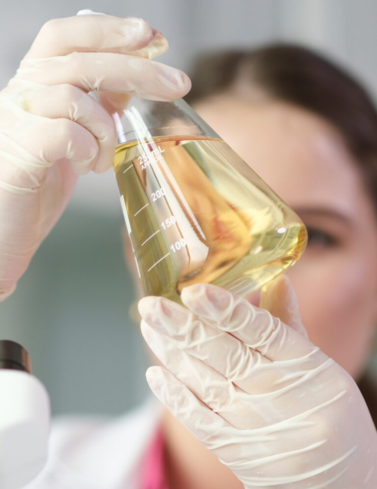 Scientist chemist looking at flask with yellow brake oil in chemistry lab closeup
